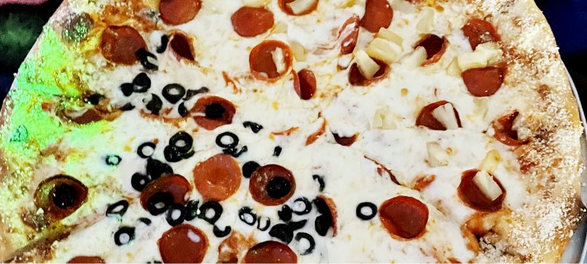 Close up shot of a half olive and half pineapple pepperoni pizza during cosmic bowling